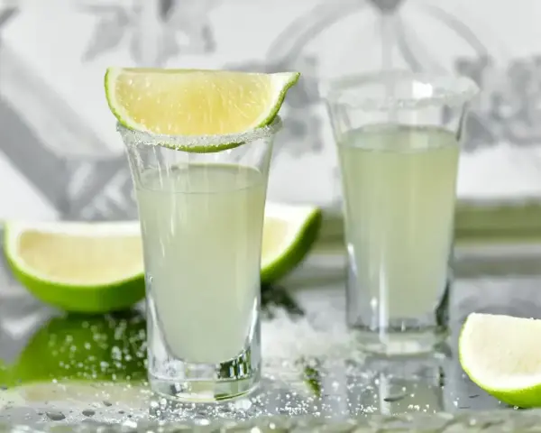 Wściekłe psy drink jak zrobić: dwa kieliszki z solą i limonką, obok ćwiartki limonki.