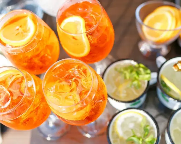 Orzeźwiający drink z prosecco, udekorowany plasterkiem pomarańczy, czeka na gości. Obok inne napoje z miętą i cytryną.