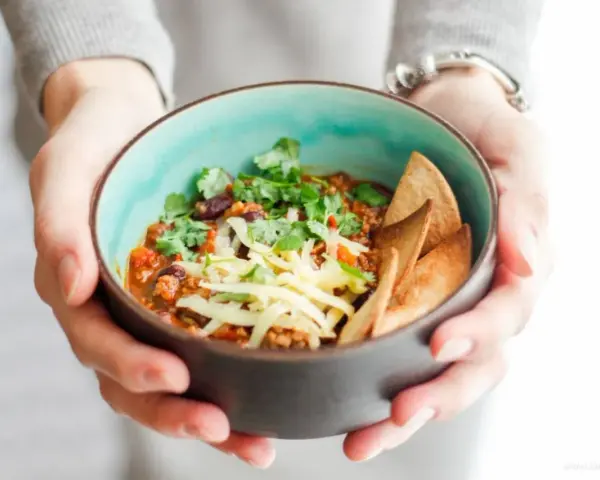 Miseczka pysznego chili con carne przepis, posypana serem i świeżą kolendrą, z chrupiącymi nachos. Idealne na chłodne dni.