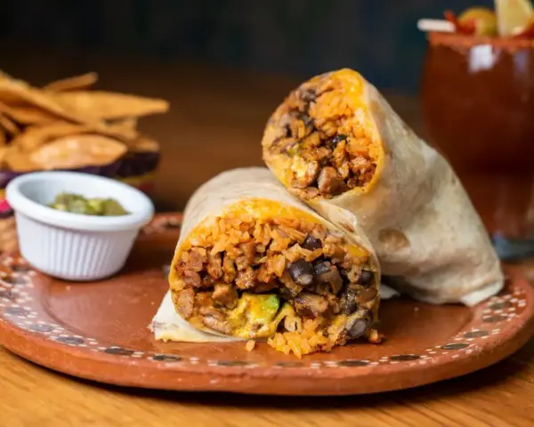 Pyszny burrito przepis: soczyste mięso, ryż, fasola i awokado zawinięte w tortillę. Obok chipsy i sos.