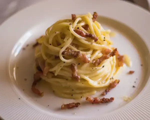 Pyszne spaghetti carbonara, idealne na prosty przepis. Kremowy sos, chrupiący boczek i czarny pieprz na talerzu.