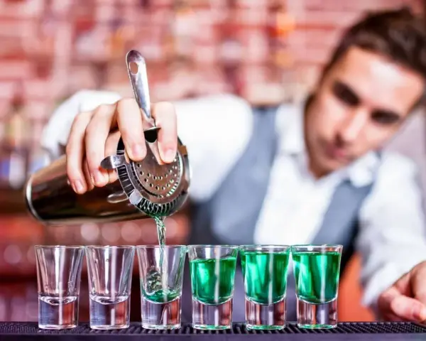 Barman nalewa zielony shot. Zastanawiasz się, ile kosztuje kurs barmana? To inwestycja w przyszłość!