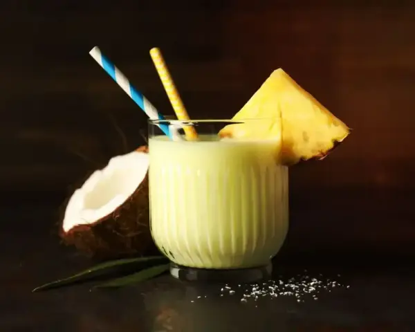 Orzeźwiający drink z mlekiem, kokosem i ananasem, ozdobiony plasterkiem owocu i kolorowymi słomkami. Idealny na tropikalne popołudnie.