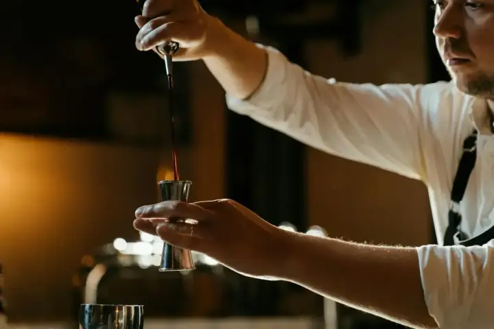 Barman nalewa ciemny płyn do jiggera, przygotowując drinka z Jägermeisterem i sokiem pomarańczowym.