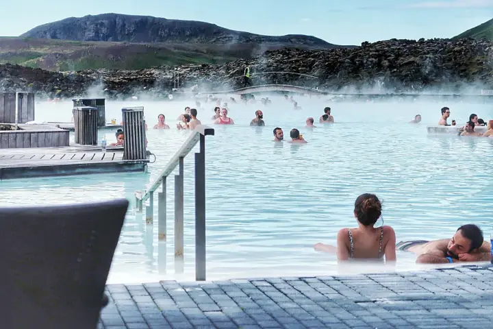 Relaks w Blue Lagoon, geotermalnym basenie z parą unoszącą się nad turkusową wodą. Ludzie kąpią się i odpoczywają.
