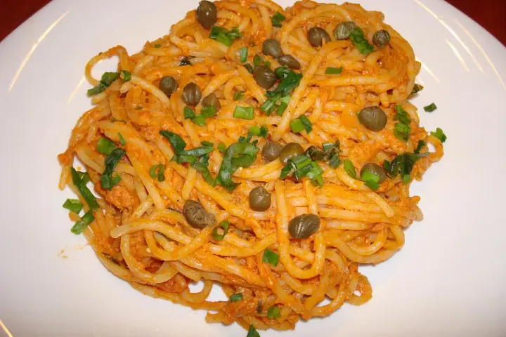 Pyszne spaghetti z tuńczykiem i kaparami, posypane szczypiorkiem, na białym talerzu.