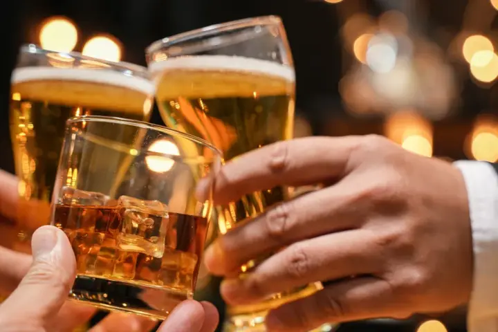 Trzy dłonie wznoszą toast: jedna z whisky na lodzie, dwie z piwem. Lepiej 2 drinki czy 2 piwa?