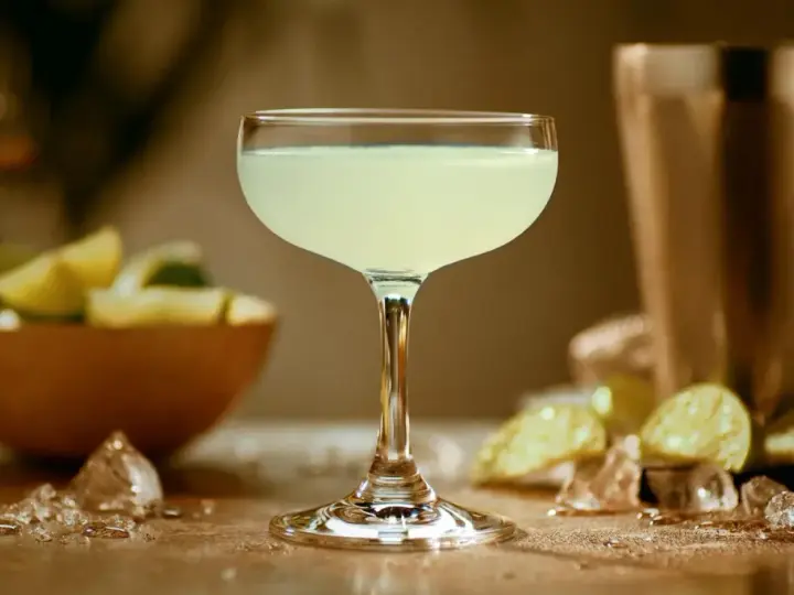 Orzeźwiający daiquiri, idealny na upalne dni. W tle miska z limonkami i kostki lodu.