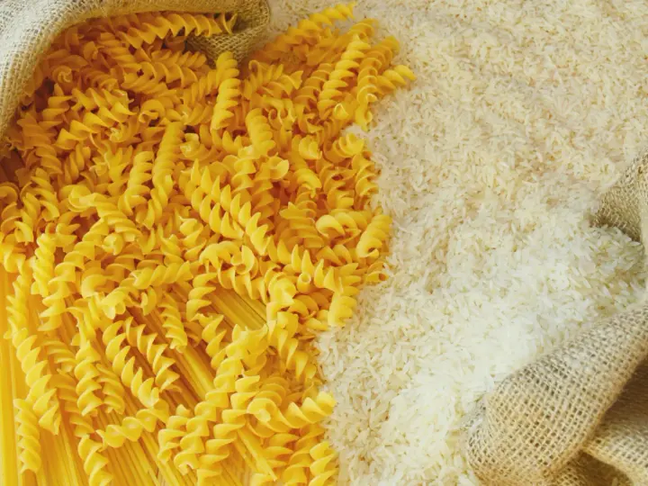 Ryż vs makaron: obok siebie leżą dwa rodzaje produktów. Z worka wysypano biały ryż, a obok niego spiralne fusilli i długie spaghetti.