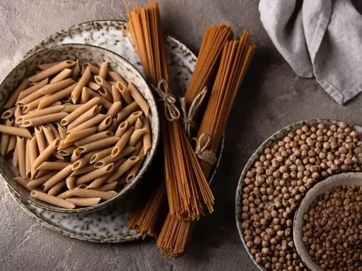 Jasny makaron penne w misce i ciemny makaron spaghetti na talerzu, obok ciecierzycy.