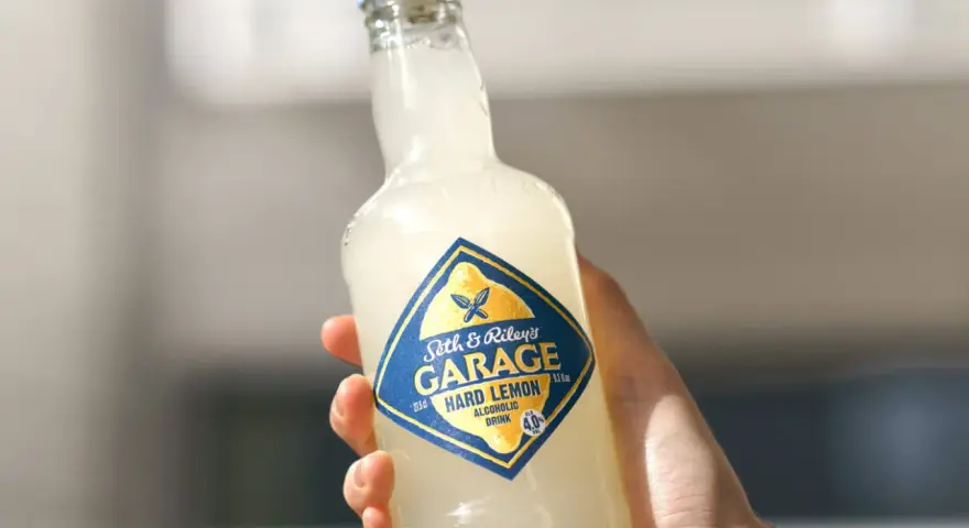 Ręka trzyma butelkę Seth & Riley's GARAGE Hard Lemon, orzeźwiający drink z piwem.