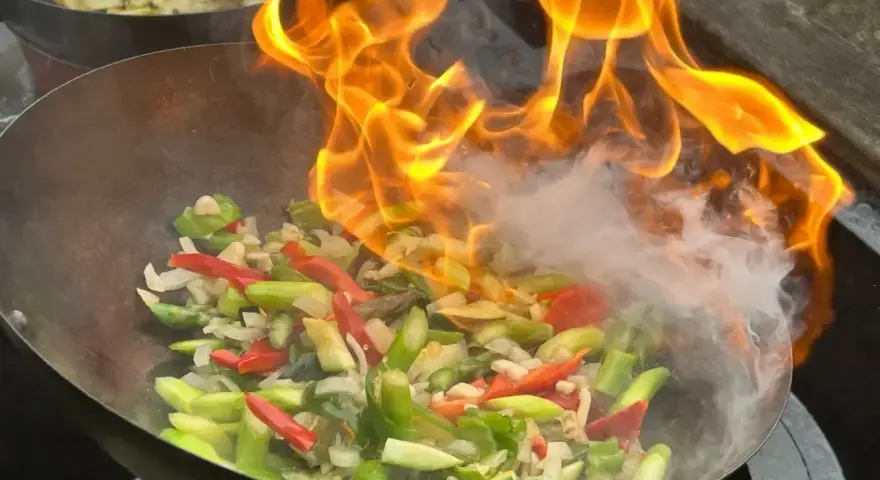 Pyszny stir-fry przepis w akcji! Warzywa w woku płoną żywym ogniem, tworząc apetyczny dym.