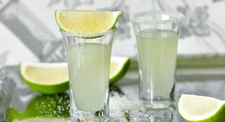 Dwa kieliszki z drinkiem Kamikadze, ozdobione solą i plasterkami limonki. Idealny przepis na orzeźwiający shot.