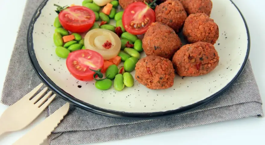 Falafel kontra kotlety sojowe: chrupiące kulki falafela i soczyste pomidorki z edamame na talerzu.