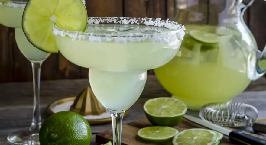 Spicy Margarita przepis: orzeźwiający drink z solą na brzegu kieliszka, limonkami i dzbankiem pełnym zielonego napoju.