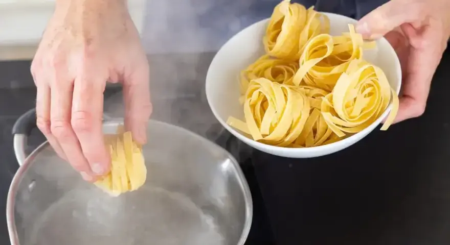 Ręka wkłada tagliatelle do wrzącej wody. Kluczowe jest, na jakim ogniu gotować makaron, by był al dente.