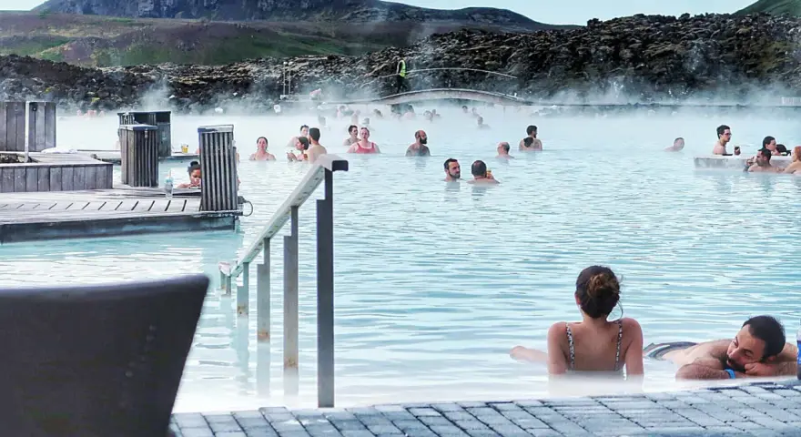 Relaks w Blue Lagoon, geotermalnym basenie z parą unoszącą się nad turkusową wodą. Ludzie kąpią się i odpoczywają.