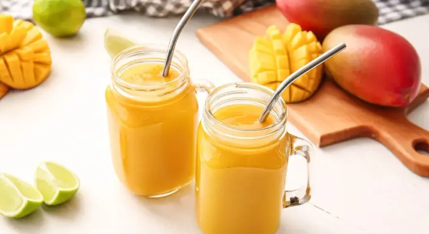 Orzeźwiający drink z wódką mango, podany w słoiczkach z metalowymi słomkami, obok świeżych owoców mango i limonek.