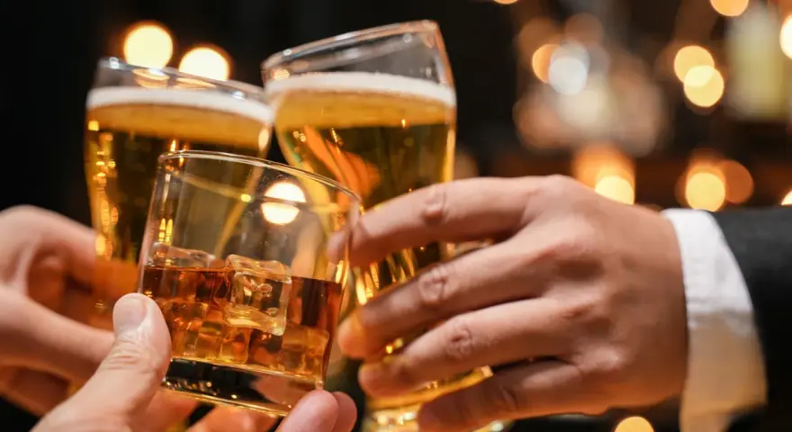 Trzy dłonie wznoszą toast: jedna z whisky na lodzie, dwie z piwem. Lepiej 2 drinki czy 2 piwa?