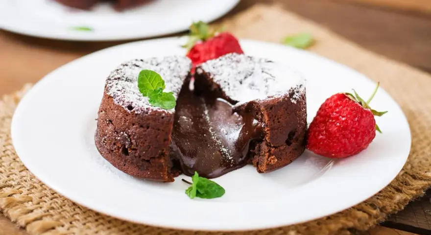 Pyszny fondant czekoladowy z płynnym środkiem, przypominający małe soufflé czekoladowe, podany z truskawkami i miętą.