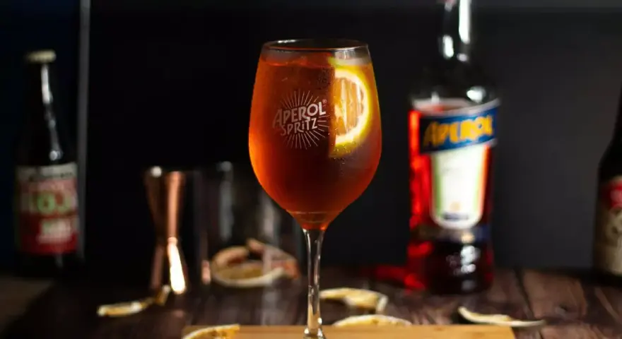 Orzeźwiający drink z aperolem i wódką, ozdobiony plasterkiem pomarańczy. Idealny na letnie wieczory.