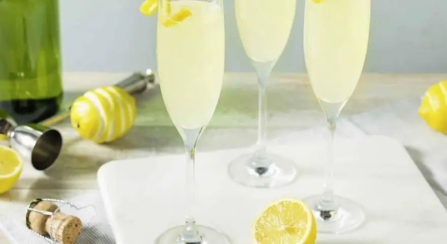 Trzy kieliszki musującego drinka French 75, jeden na ginie, drugi na koniaku, z cytrynową dekoracją.