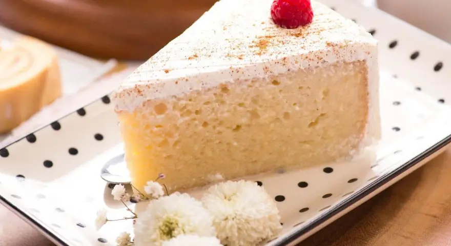 Pyszny kawałek ciasta Tres Leches, udekorowany maliną i cynamonem, czeka na spróbowanie. Idealny przepis na deser.