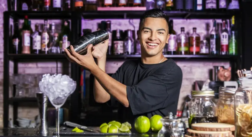 Uśmiechnięty barman miesza drinka. Chcesz wiedzieć, jak zostać barmanem kobietą? Zacznij od nauki sztuki miksowania!