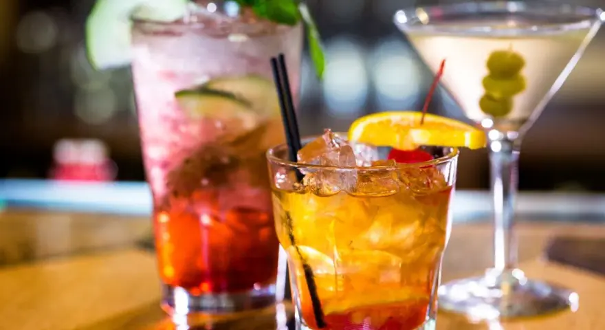 Kolorowe drinki z wódką smakową: czerwony z ogórkiem i miętą, bursztynowy z pomarańczą i wiśnią, oraz martini z oliwkami.