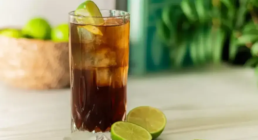 Orzeźwiający Cuba Libre, czyli rum z colą i limonką, z kostkami lodu i świeżymi limonkami w tle. Idealny na upalne dni.