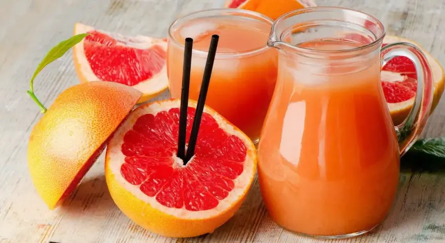 Orzeźwiający drink z grejpfrutem, podany w dzbanku i szklance, otoczony świeżymi owocami. Idealny na upalne dni.