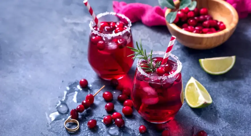 Dwa orzeźwiające drinki z grenadiną, ozdobione żurawiną i rozmarynem, z limonką w tle.