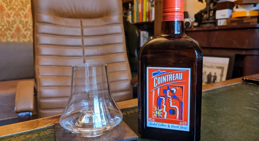 Cointreau kontra Triple Sec w koktajlach: butelka Cointreau i pusty kieliszek na biurku.