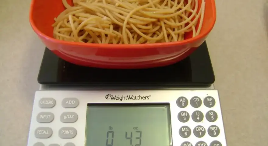 Ugotowany makaron w czerwonej misce na wadze cyfrowej pokazującej 0.43 funta.