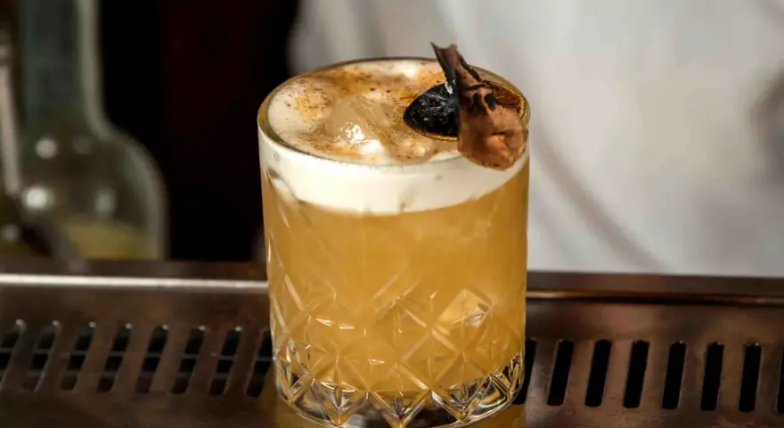 Elegancki Whisky Sour i Amaretto Sour z pianką i dekoracją na barze.