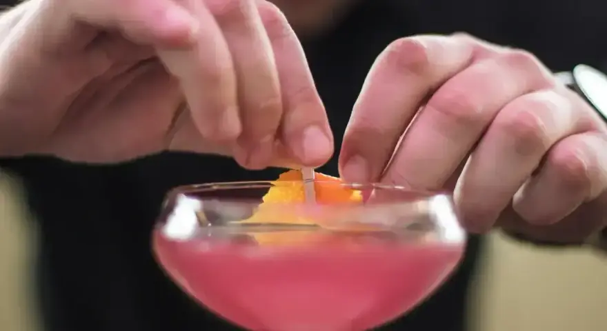 Ręce dekorują drinka skórką pomarańczy. To ostatni krok w przygotowaniu Cosmopolitan przepis.