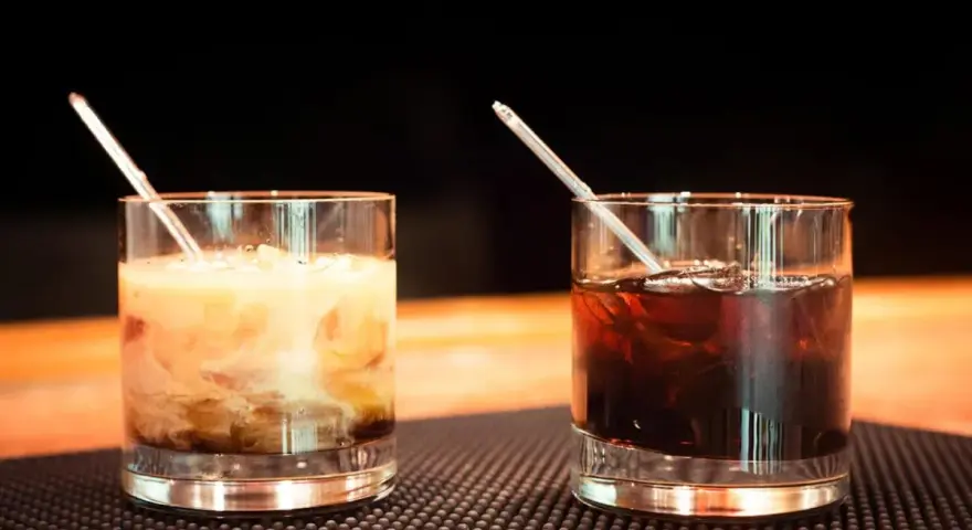 Dwa drinki z likierem kawowym na barze. Jeden kremowy, drugi ciemny, oba z lodem i słomką.