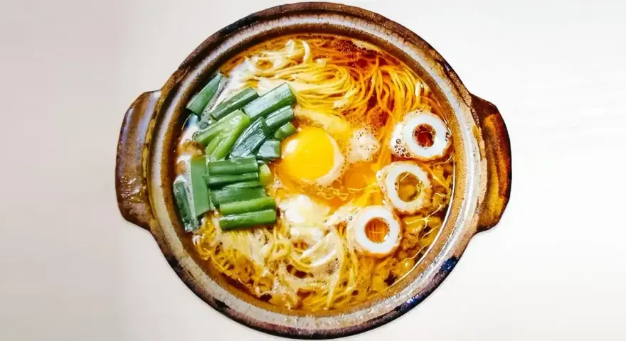 Gorący garnek z aromatycznym bulionem, żółtkiem jajka, zielonym szczypiorkiem i krążkami rybnymi. Czy to ramen czy udon?