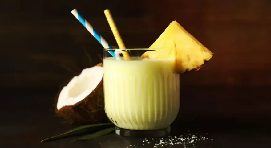 Orzeźwiający drink z mlekiem, kokosem i ananasem, ozdobiony plasterkiem owocu i kolorowymi słomkami. Idealny na tropikalne popołudnie.