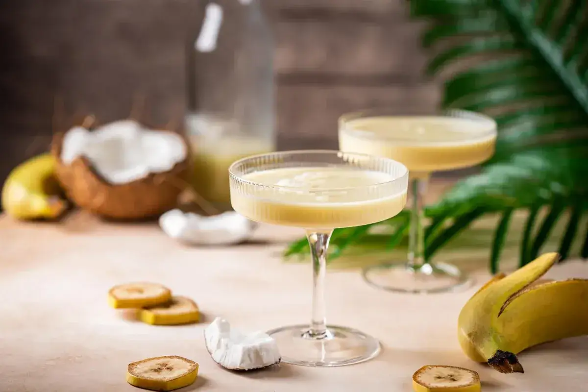 Kremowy drink z likieru bananowego, podany w eleganckich kieliszkach, z dodatkiem kokosa i plasterków banana.