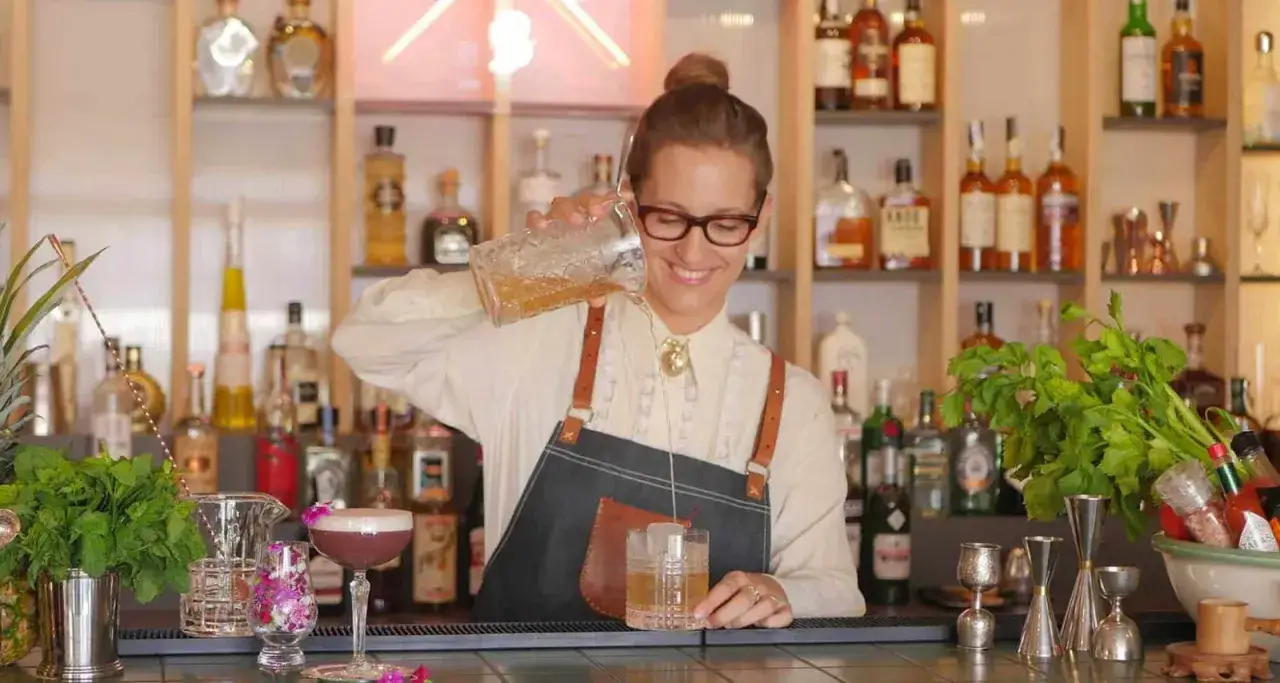 Uśmiechnięta barmanka przygotowuje drinka. Zastanawiasz się, ile zarabia barman za granicą?