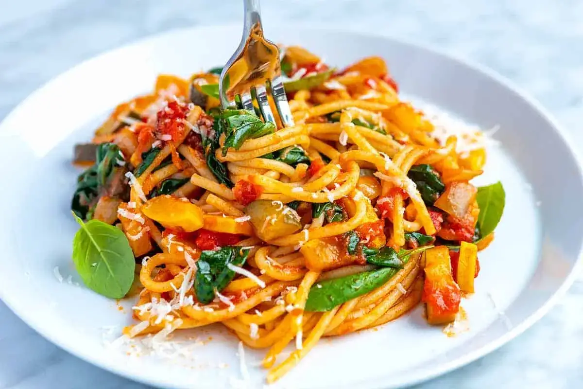 Makaron spaghetti z cukinią, pomidorami i szpinakiem, posypany parmezanem. Pyszne danie warzywne.