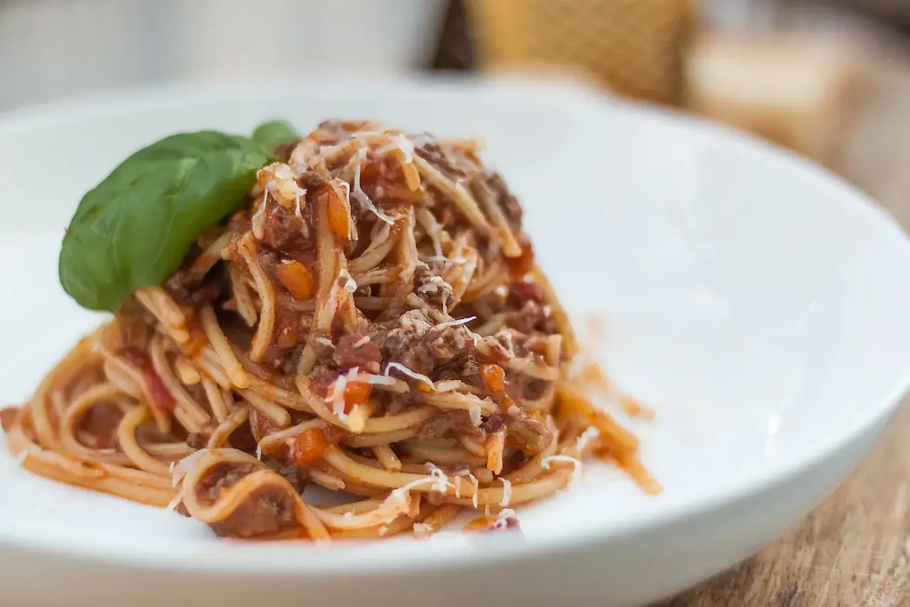 Pyszne Spaghetti Bolognese przepis na talerzu, udekorowane listkiem bazylii i startym parmezanem.