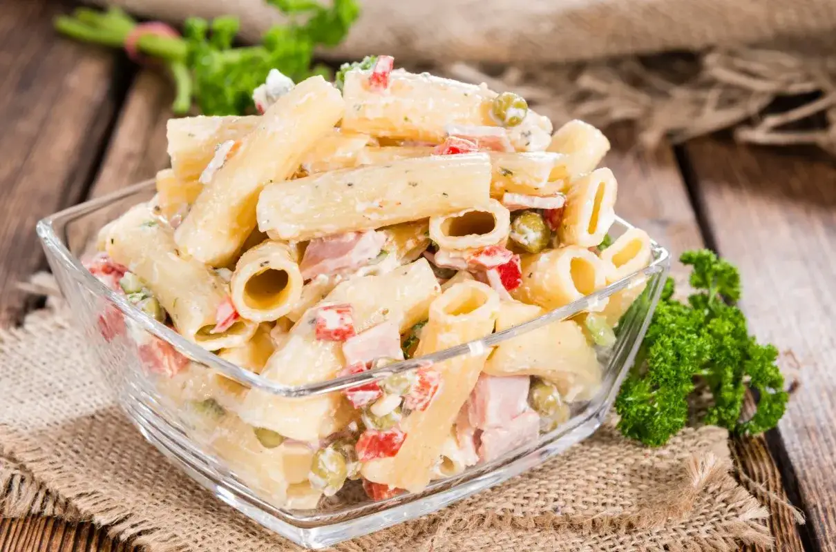 Pyszna sałatka z makaronem penne i szynką, z dodatkiem groszku i papryki, w kremowym sosie.