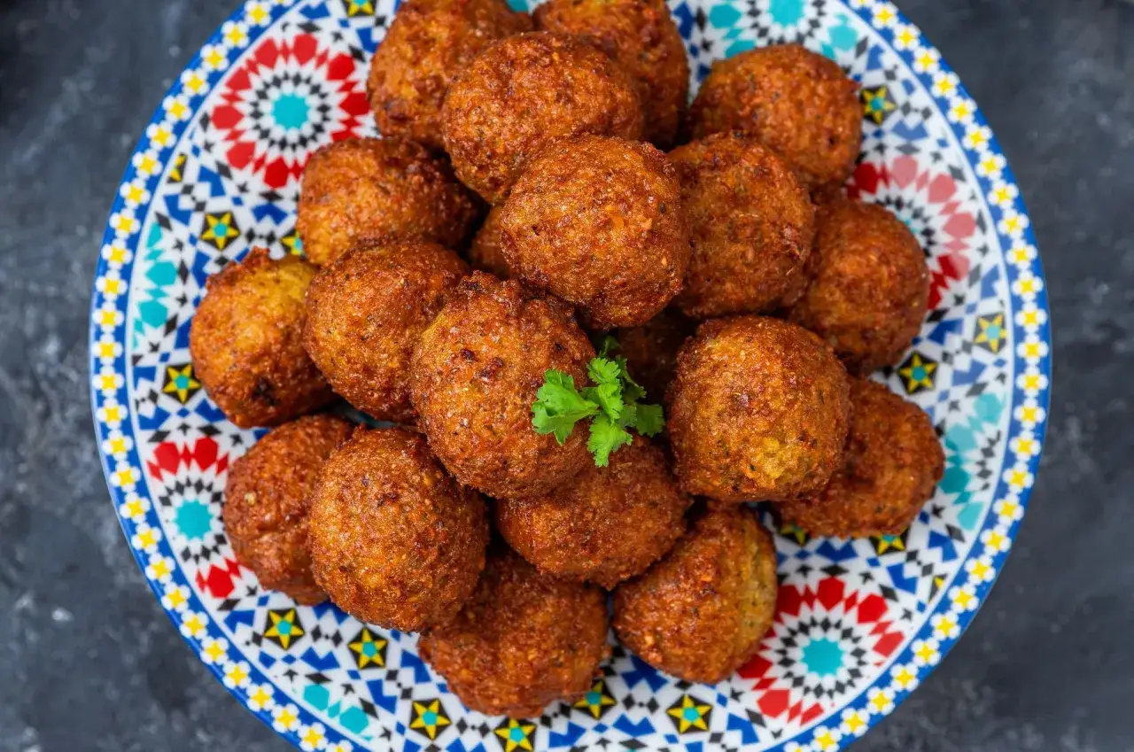 Złociste kulki falafel, idealne do przygotowania według prostego przepisu, ułożone na kolorowym talerzu z orientalnym wzorem.