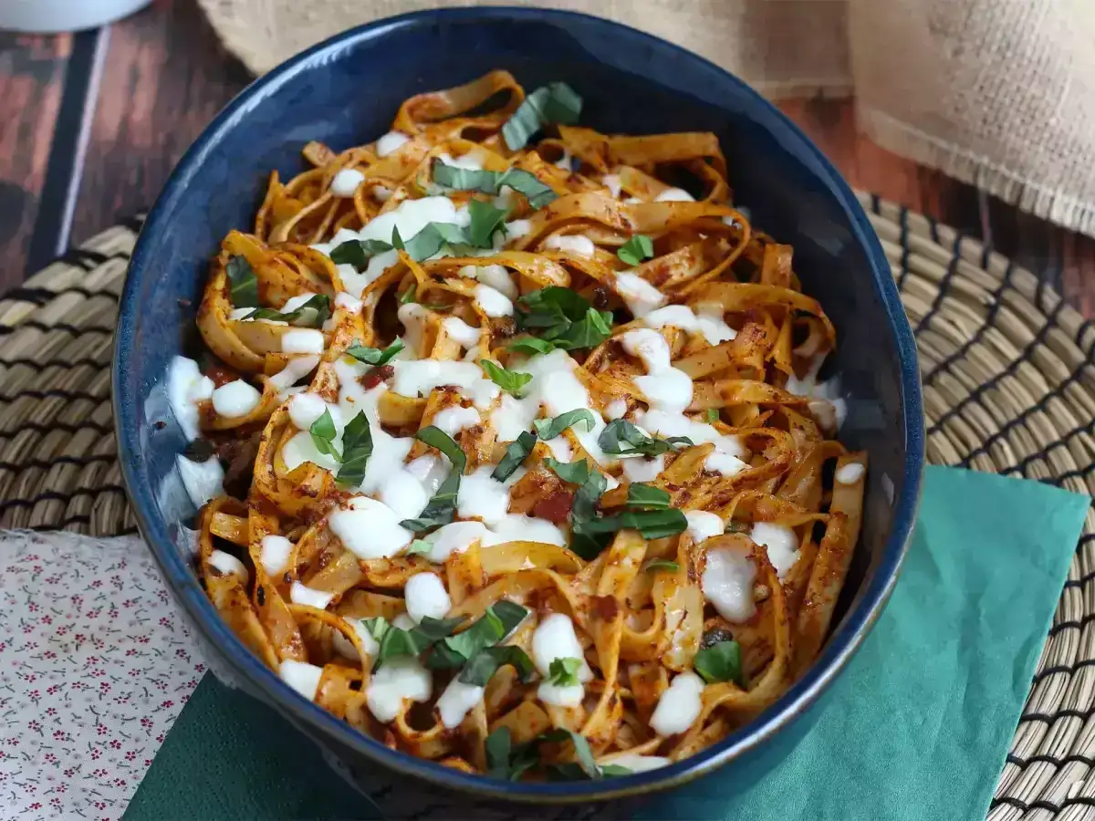 Szybki obiad z niczego: tagliatelle w sosie pomidorowym z mozzarellą i bazylią, podane w niebieskiej misie.
