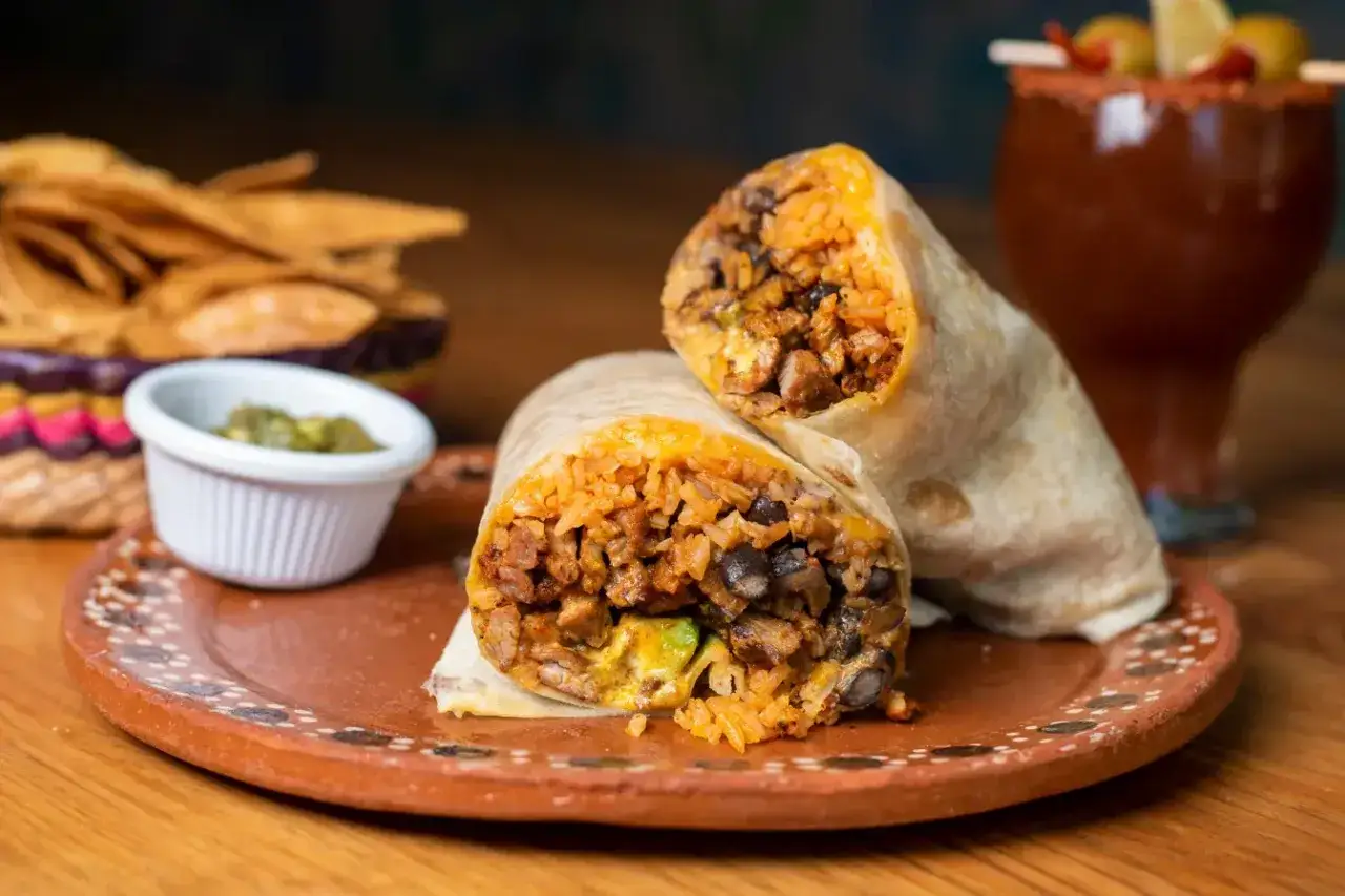 Pyszny burrito przepis: soczyste mięso, ryż, fasola i awokado zawinięte w tortillę. Obok chipsy i sos.