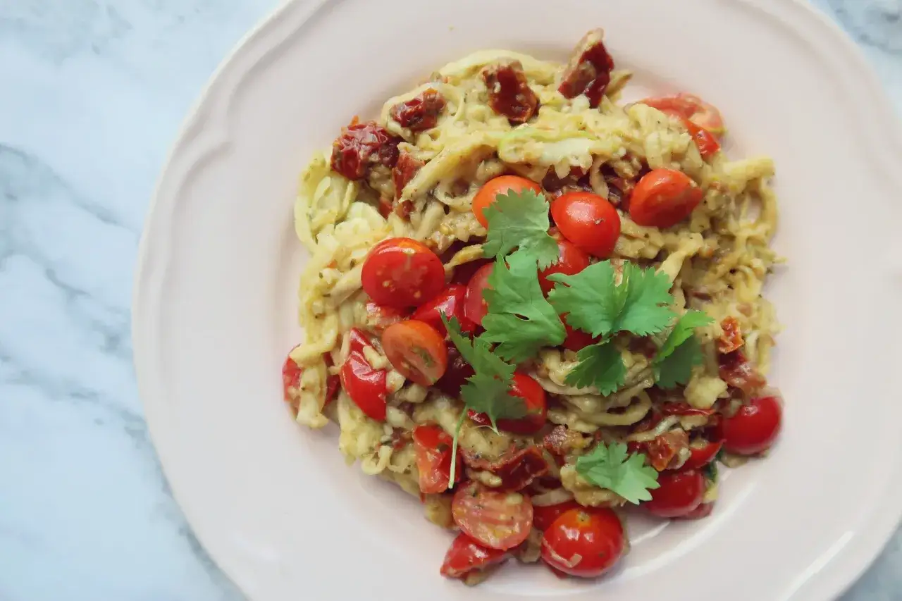 Pyszne spaghetti z cukinii z pomidorkami koktajlowymi i suszonymi pomidorami, udekorowane świeżą kolendrą.
