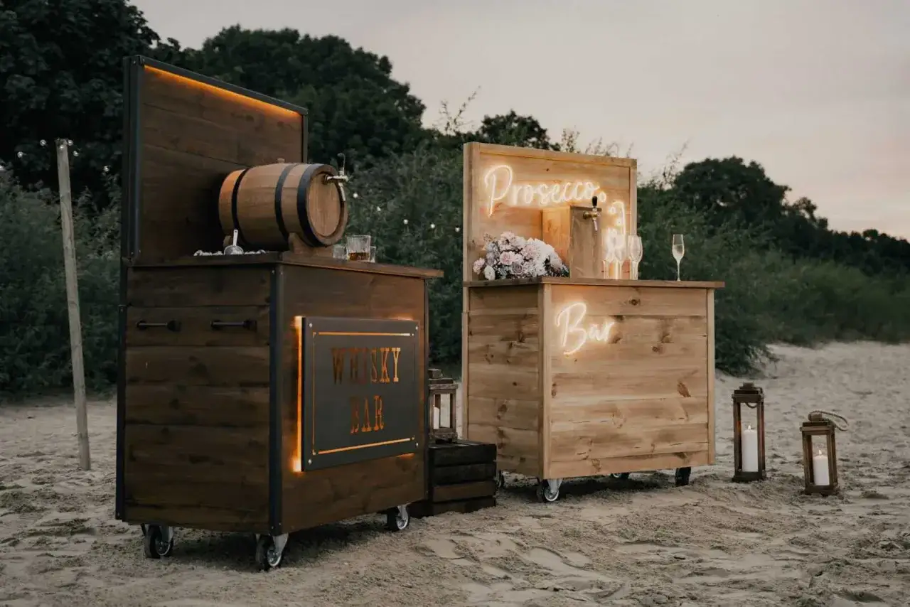 Drewniane bary weselne na plaży: jeden z beczką whisky, drugi z napisem 