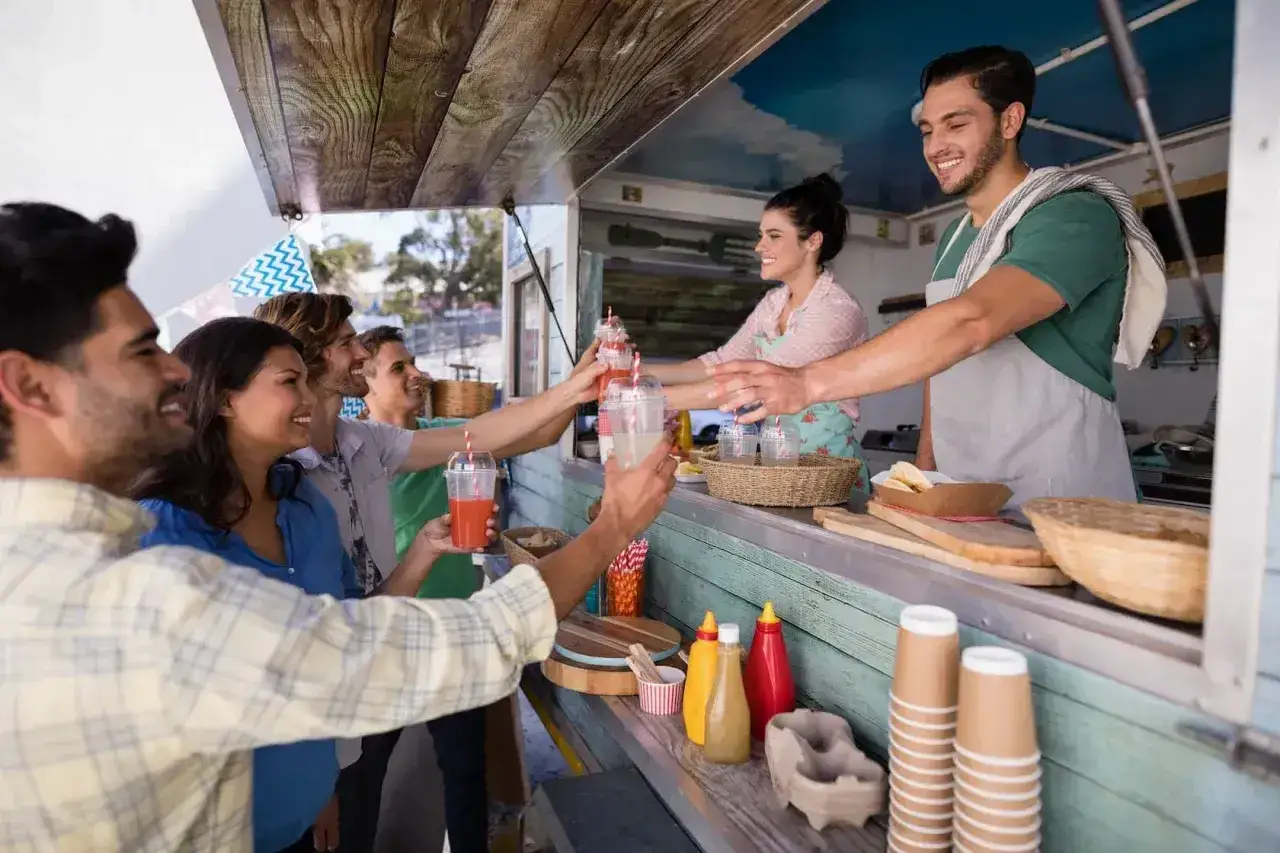 Uśmiechnięci klienci odbierają napoje od barmana w food trucku. Ciekawe, ile zarabia barman w Toruniu za taką obsługę!